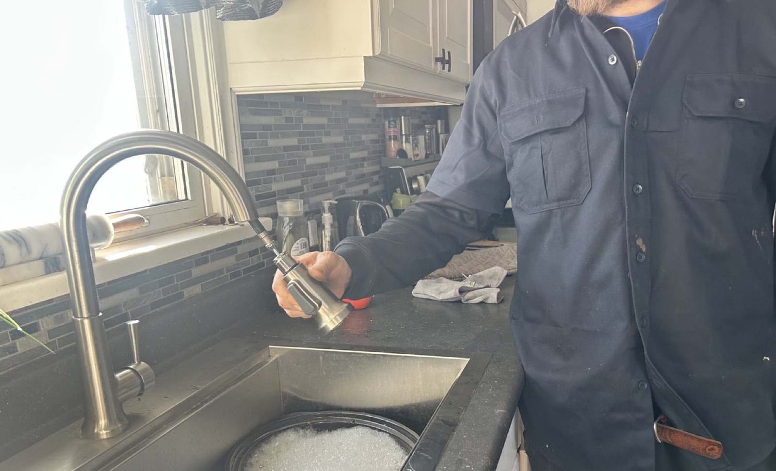 Plumber working under a kitchen sink during a sink repair in the Niagara Region