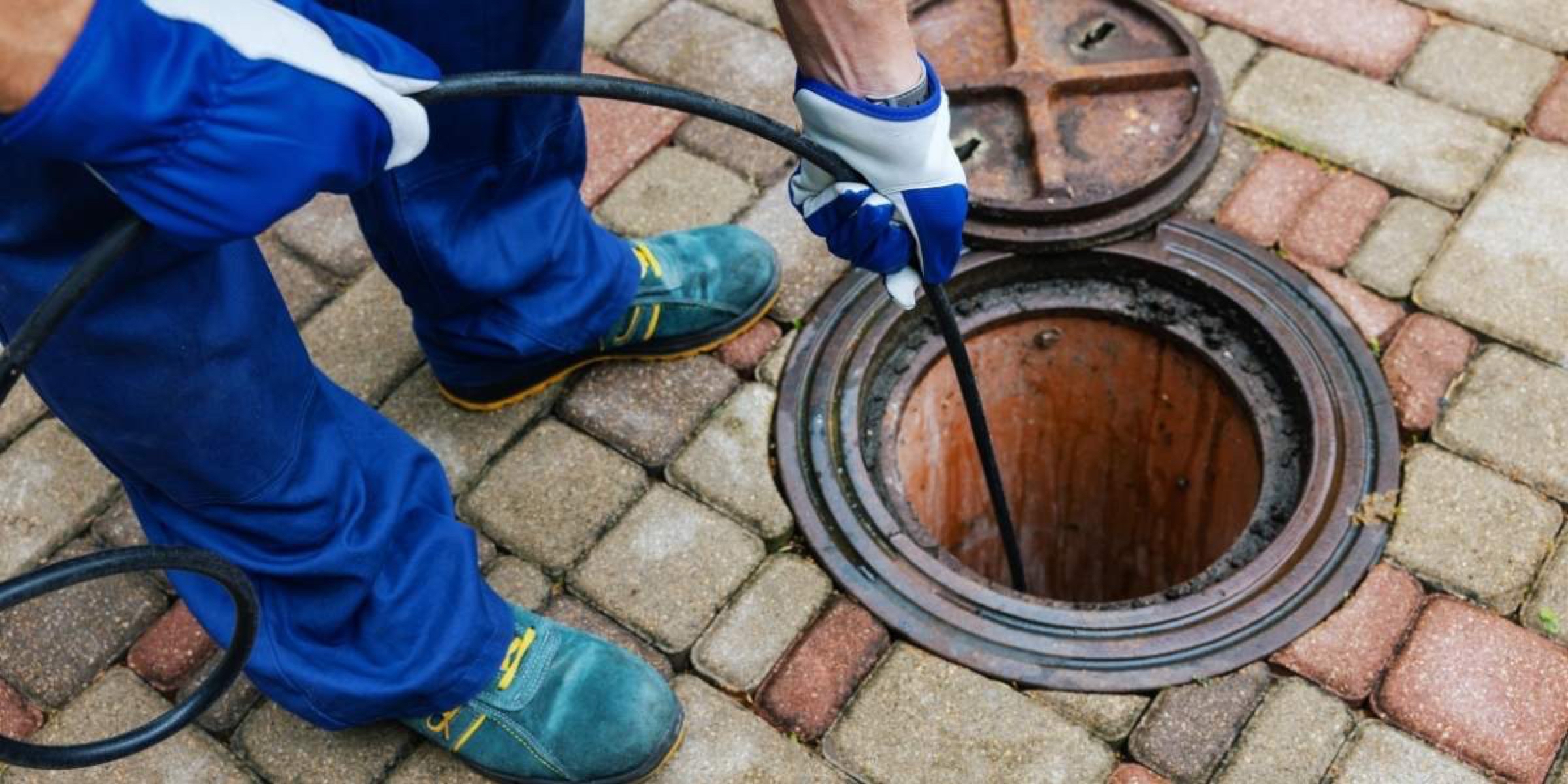 Plumber feeding a drain cleaning cable into an open sewer access in the Niagara Region